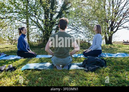 Three Friends Practicing Yoga Meditation Outdoors in a Sunny Park Stock Photo
