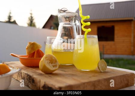 A refreshing lemonade is being served on an outdoor patio, featuring a wooden cutting board and a ceramic bowl. The close-up view highlights sliced lemons and a pitcher of lemonade. Stock Photo