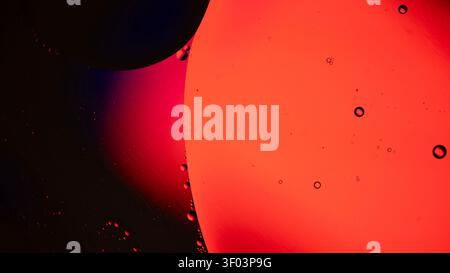 Extreme close up of red and orange liquid droplets on a dark background, showing glossy spheres, smooth surfaces, and vivid color Stock Photo