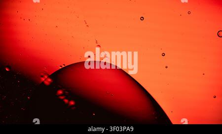 Close-up image featuring an orange background with a dark curved silhouette and scattered liquid droplets Stock Photo