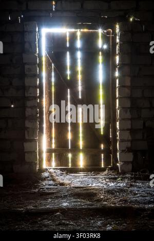 Rays of light shine through the plank door of an old barn. An old door in a brick doorway. Stock Photo