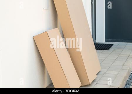 Two brown cardboard delivery boxes leaning against a wall near the front door of a home.  Stock Photo