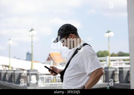 BANGKOK, THAILAND - JUN 3, 2026: Man in black cap using smartphone, side profile. Stock Photo