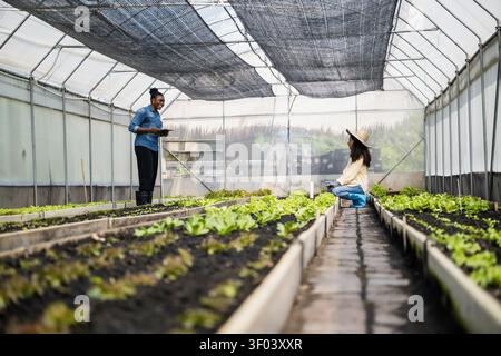 Mother teaching daughter gardening in greenhouse, Learn practical skills with mother while using modern technology in tablet step info smart farmer ne Stock Photo