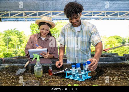Smiling agricultural students collect soil samples with test tubes and note for soil analysis in agricultural laboratory for farm science project. Sma Stock Photo