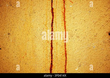 Yellow textured wall showing two vertical rust stains on a weathered plaster surface, conveying age, decay and industrial character. Close-up detail e Stock Photo