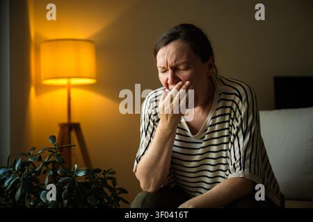 Tired woman yawning at home after a long day. Fatigue, work-life balance, evening routine and healthy rest concept. Selective focus. Stock Photo