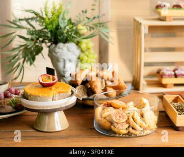 A snacks table displays a passion fruit spread on a stand alongside bruschetta and pastries, styled with greenery in a decorative bust vase Stock Photo