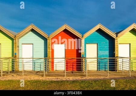 Colorful wooden beach huts & cabins with white doors under a clear blue sky Blyth northumberland Stock Photo