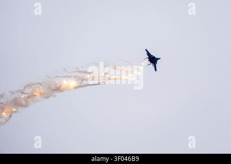 A military fighter plane flies in the sky and releases false thermal targets, traps for air defense missiles. an aviation show in the sky. aerobatics Stock Photo