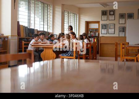 Elementary School Students Reading Together in a School Library with Teacher Supervising Stock Photo
