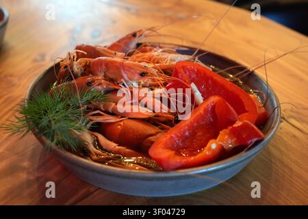 Boiled crawfish served with red bell pepper and fresh dill in a gray ceramic bowl. Summer seafood dish and rustic restaurant appetizer. Stock Photo
