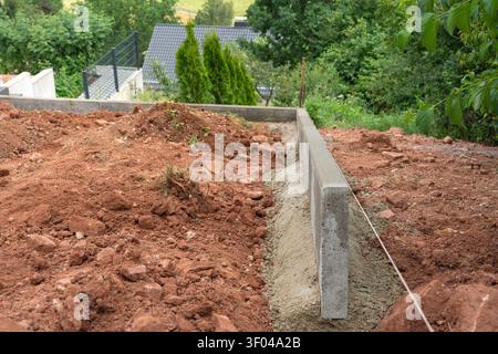 Concrete foundation construction in progress, in residential area, with concrete blocks, red soil, greenery, with concrete, soil texture, from a Stock Photo