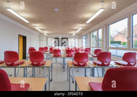 A modern, completely empty school classroom featuring red chairs placed on top of wooden desks Stock Photo