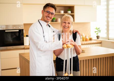 A doctor stands beside a senior patient, providing reassurance as she confidently uses mobility aids in her home. Stock Photo