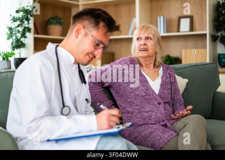 A healthcare professional carefully documents an elderly patient's concerns as she discusses her health issues during an in-home medical appointment. Stock Photo