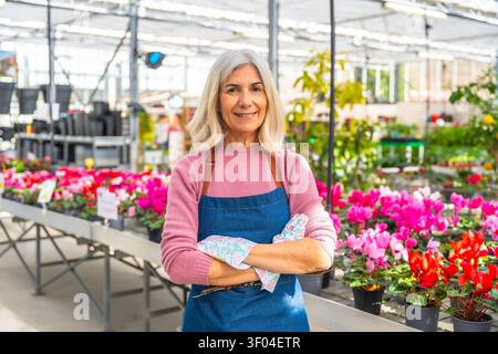 Smiling senior woman gardener posing in flower greenhouse Stock Photo
