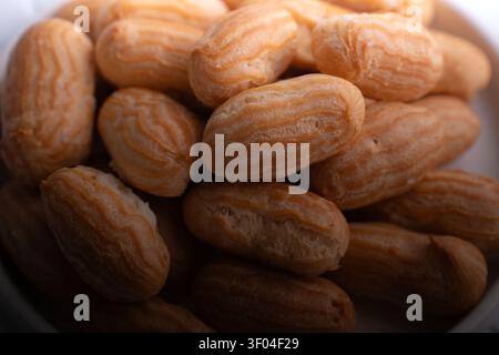 macro close-up of golden-brown mini éclairs (choux pastries) piled in a bowl on a warm countertop, showing textured ridges, flaky crust, soft lighting Stock Photo