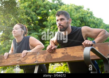 Athletic Man and Woman Doing Incline Push-Ups on a Park Bench During an Outdoor Workout Stock Photo