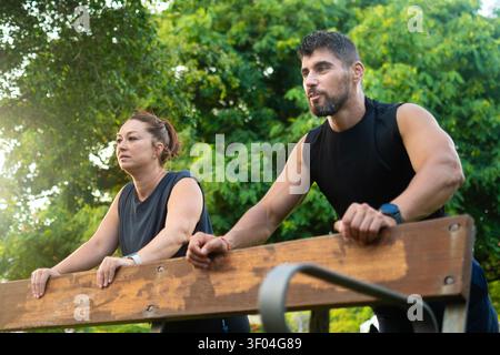 Athletic Man and Woman Doing Incline Push-Ups on a Park Bench During an Outdoor Workout Stock Photo