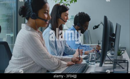 Three diversity business operators talking working in callcenter. African American woman agent talk chat with client writing notes smiling write data Stock Photo