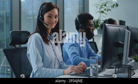Happy Caucasian business woman working in call center businesswoman talking looking at camera smiling posing at table near multiethnic colleagues Stock Photo