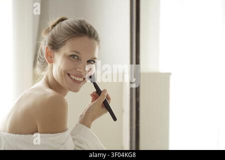 Smiling woman in a robe applying makeup Stock Photo