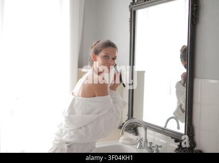 Woman in bathrobe applying makeup in mirror Stock Photo