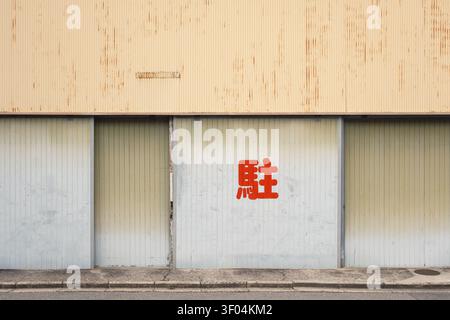 Minimalist exterior wall of a building with closed metal shutters and a single red kanji character script, Kyoto, Japan Stock Photo