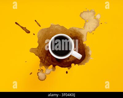 Coffee cup spilling dark liquid and creating a brown stain on a vibrant yellow background, viewed from top. Messy morning Stock Photo
