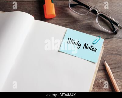 Study notes text on a note paper clipped to an open book on a wooden desk. Stock Photo