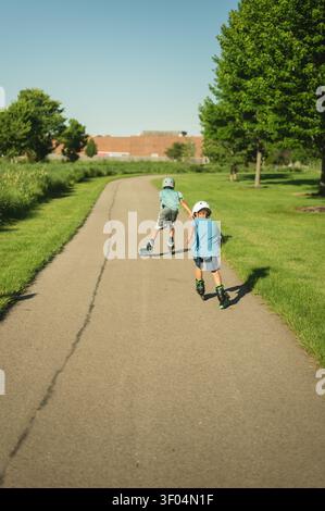 Backview of two boys rollerblading on a sunny park path Stock Photo