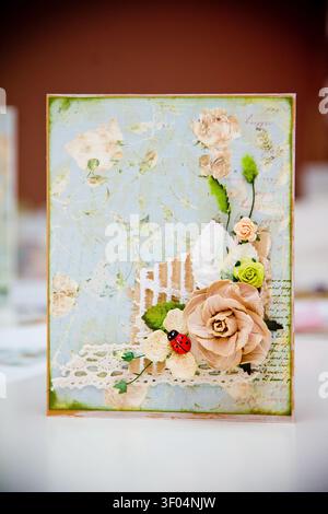 Handmade card featuring layered paper flowers in pink white green with lace trim vintage script background. Soft lighting highlights delicate textures Stock Photo