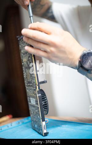 Person repairs a computer graphics card in a workshop during the day using tools for maintenance and improvement Stock Photo
