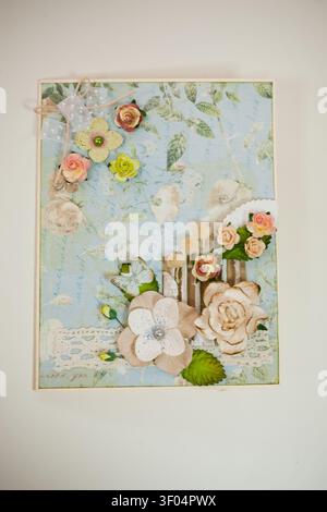Handmade card featuring layered paper flowers in pink white green with lace trim vintage script background. Soft lighting highlights delicate textures Stock Photo