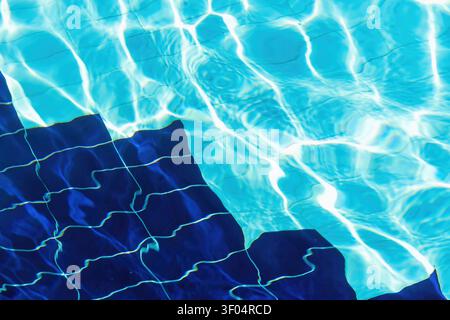 Crystal clear swimming pool water with sunlit ripples over blue tiles. Vibrant abstract background for summer travel, luxury resorts, and wellness Stock Photo