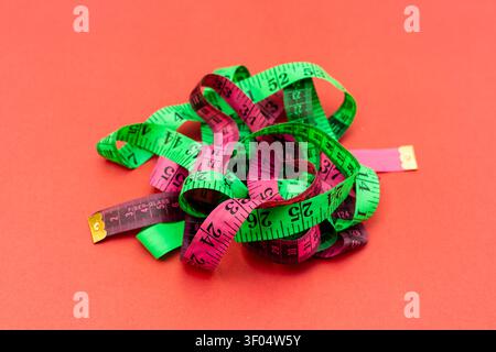 Green and Pink Measuring Tape Tangled on Red Background for Tailoring and Fitness Concept. Stock Photo