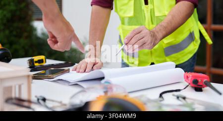 Cropped hands of architects pointing at blueprints on construction site table Stock Photo