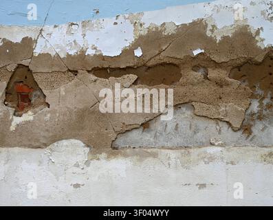 Horizontal close up of a decaying wall surface with light blue and white paint chipped cracked and worn away, revealing concrete layers Stock Photo