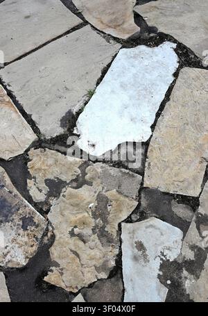 Vertical close up of flat slate flagstone surface, with black dirt scattered between tan, grey, and white slate pieces Stock Photo