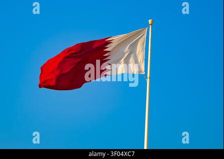 Qatar national flag waving on flagpole against clear blue sky Stock Photo