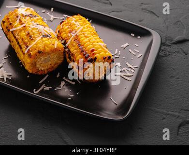 Grilled corn cobs topped with grated cheese, presenting a delicious summer snack Stock Photo
