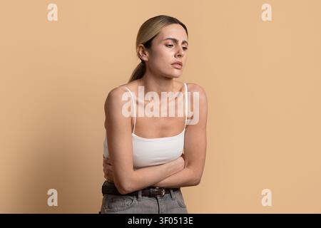 Young beautiful woman holding her stomach with worried expression on beige background Stock Photo