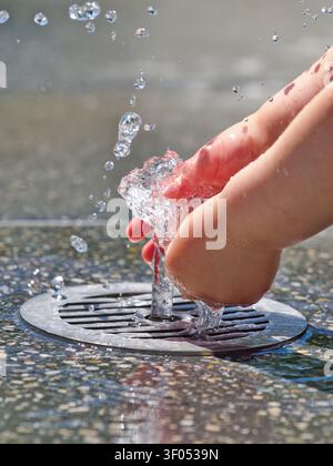 Child playing with water from a ground fountain on a sunny summer day at a public splash pad in Bavaria, Germany. Stock Photo