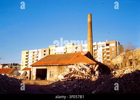 Former factory and chimney awaiting demolition, surrounded by ruins with a new apartment building behind, captured on analog film in winter. Stock Photo