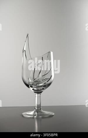Shattered goblet with sharp glass pieces reflecting fragility and destruction on a dark surface Stock Photo