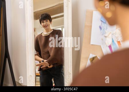 Designer looking in mirror while adjusting brown top Stock Photo
