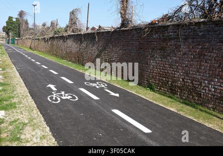 Two lane bike lanes with bicycle symbol on asphalt and dividing line. Long brick wall on the right, grass on the left. Background for copy space. Stock Photo