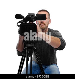 A professional videographer operates a video camera mounted on a tripod against a white background. Stock Photo