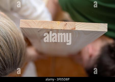 Close-up of a wooden shelf viewed during assembly with a couple working in the background. Concept of handmade furniture, teamwork, custom woodworking Stock Photo